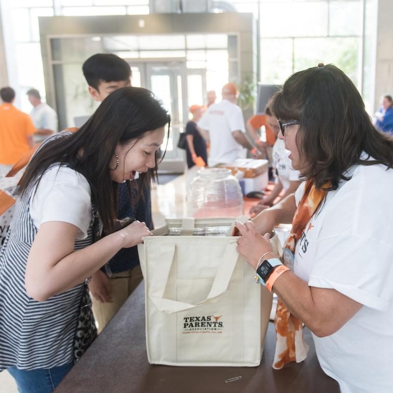 UT Austin Texas Parents new member looking in tote bag with volunteer