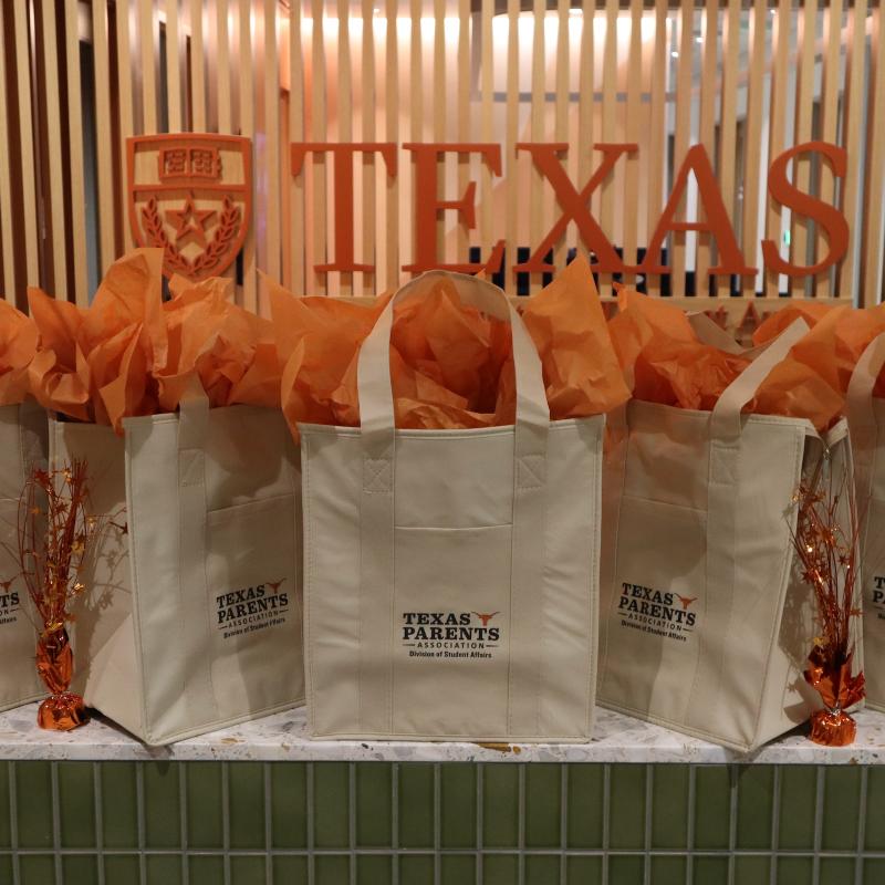 Tote bags with orange tissue in front of UT Austin logo